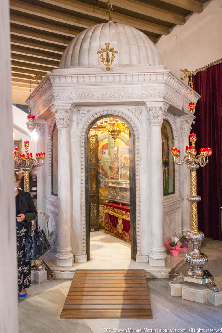 White marble shrine with arched opening, carved columns, red lamps, and candle stands.