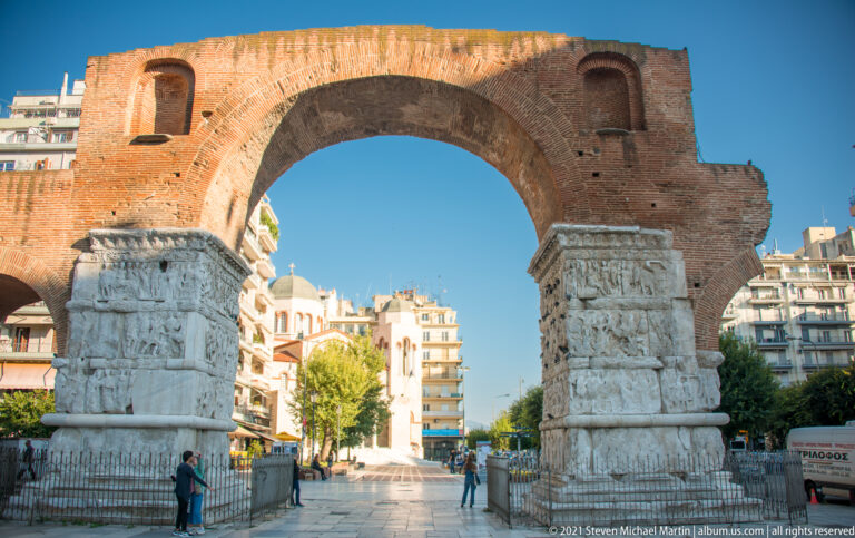 Large brick arch of Galerius supported by carved marble piers over a pedestrian area in Thessaloniki.