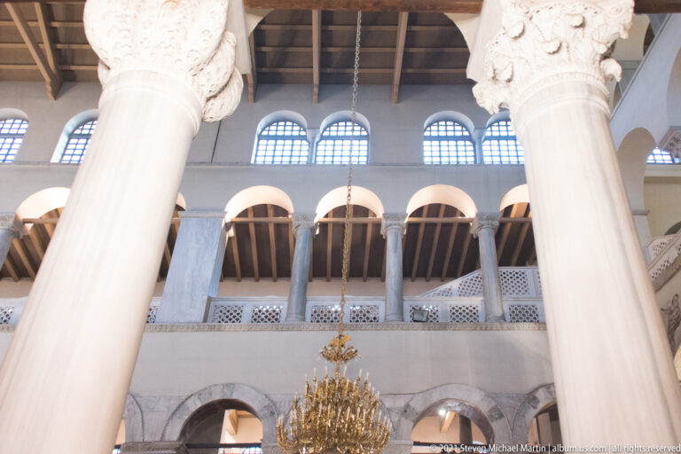 Upward view of marble columns, carved capitals, arcaded galleries, and clerestory windows.