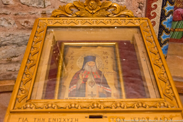 Framed icon of a bearded Orthodox cleric in dark vestments behind glass.