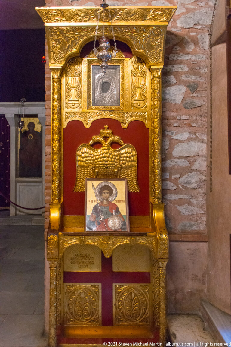 Gilded red ceremonial chair with a double-headed eagle, small icon, and framed image above.