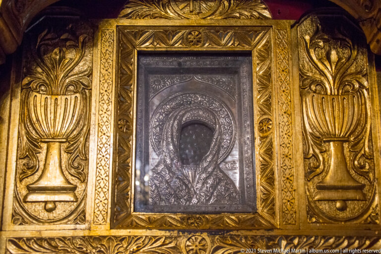 Dark metal relief icon of the Virgin and Child set in an ornate gilded frame.