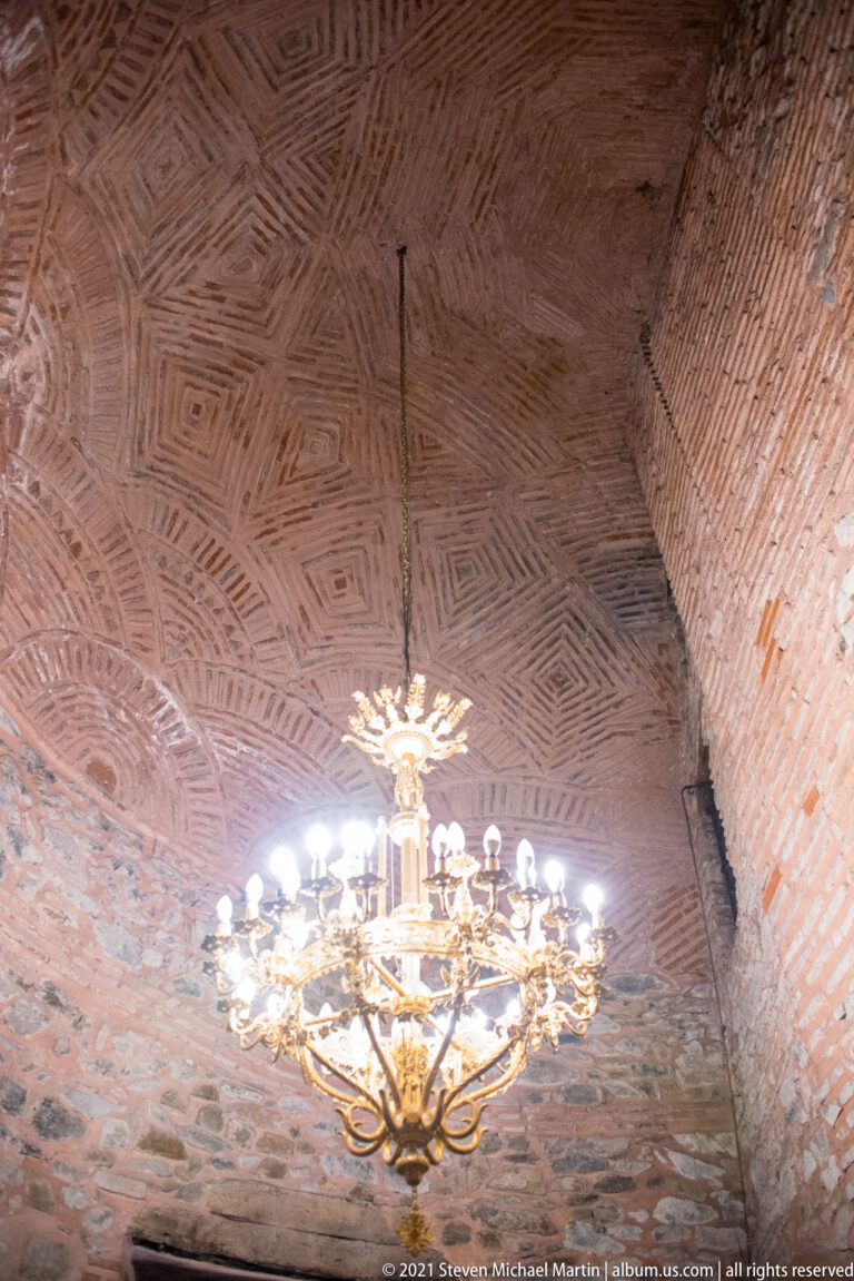 Large chandelier hanging below a patterned herringbone brick vault.