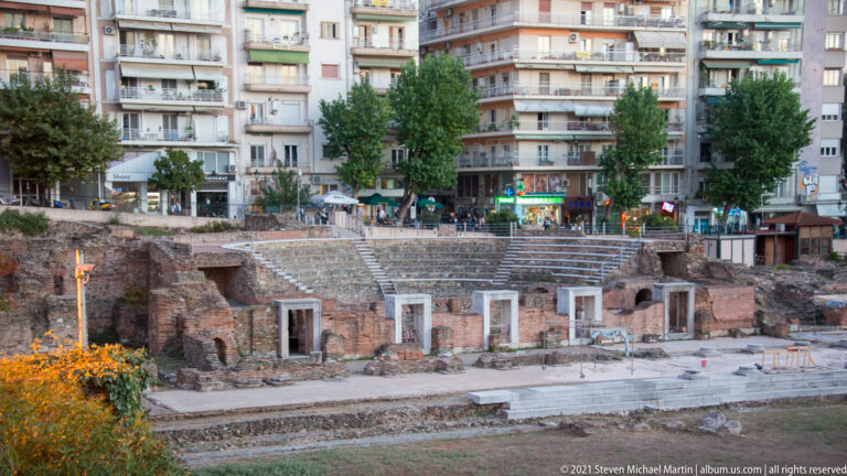 Semicircular ancient seating and brick ruins below modern apartment buildings in Thessaloniki.