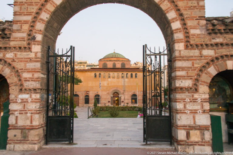 Hagia Sophia seen through an open iron gate and large brick archway in Thessaloniki.