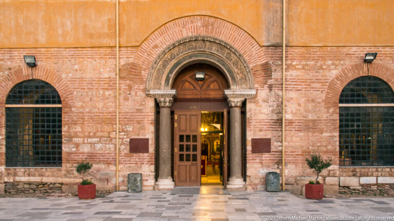 Arched entrance of Hagia Sophia with columns, carved capitals, brickwork, and glowing interior beyond.