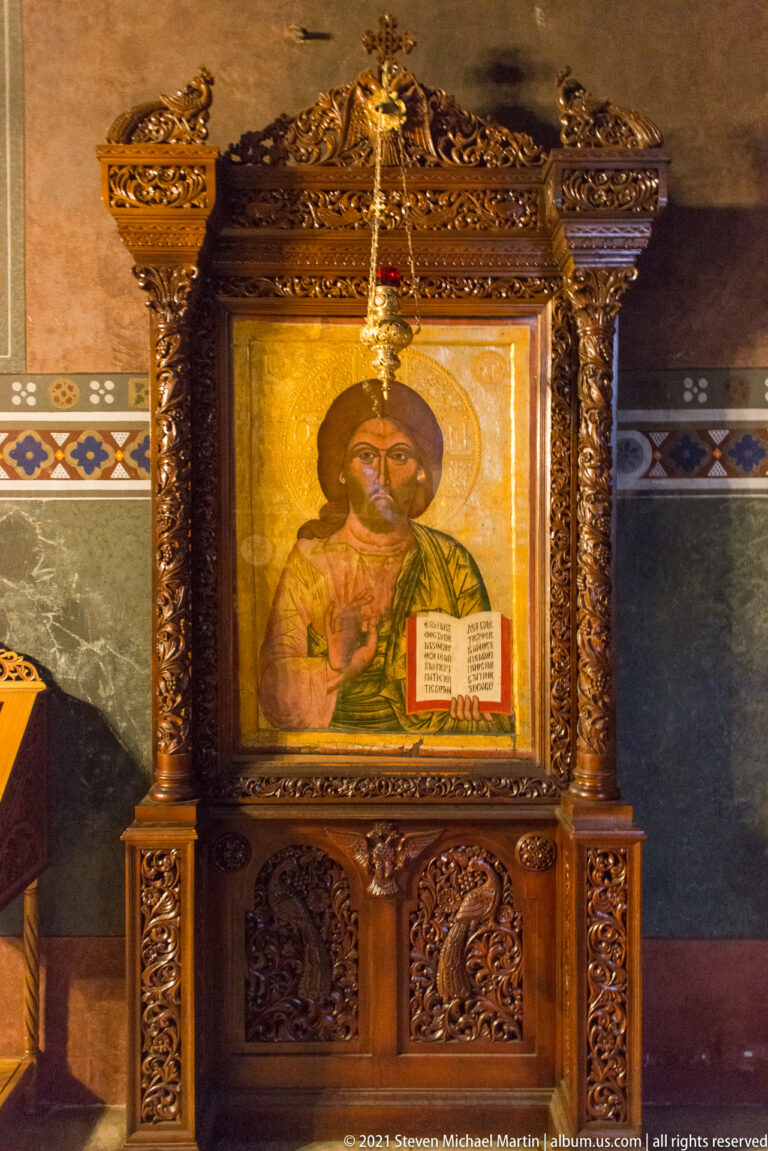 Icon of Christ Pantocrator with raised blessing hand and open Gospel in an ornate wooden frame.