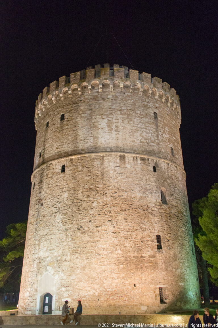 Low-angle nighttime view of the White Tower with visitors seated near its base.