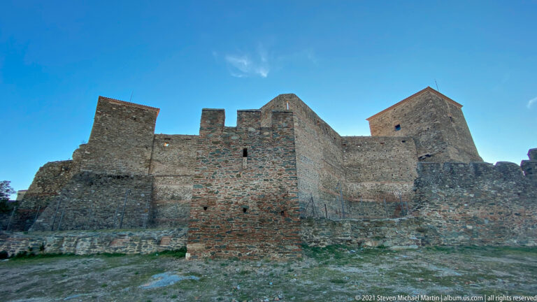 High stone-and-brick fortress walls with square towers under a clear blue sky.