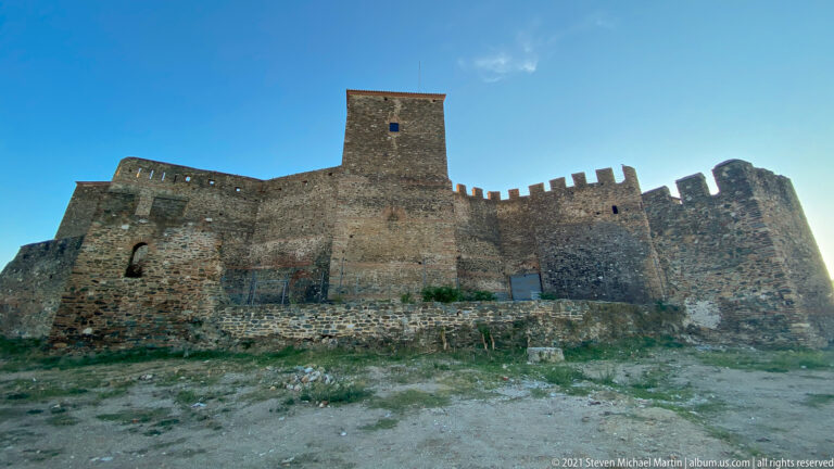 Frontal view of crenellated stone fortress walls with a tall square tower at center.