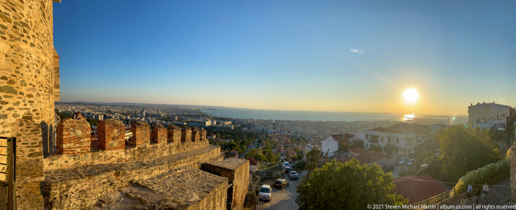 Sunset over Thessaloniki and the Thermaic Gulf beside crenellated upper-city walls.