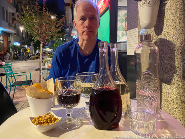 Diner at an outdoor table with red wine, water, bread, and nuts on a Thessaloniki street.