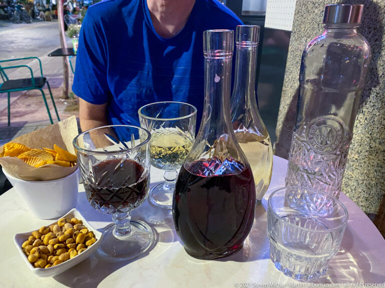 Close view of red wine, water bottle, bread, and nuts on an outdoor café table.