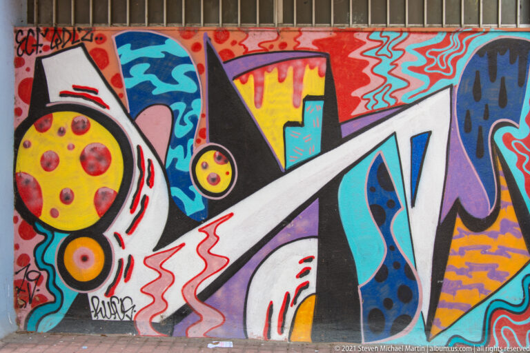 Colorful abstract street mural with circles, zigzags, angular shapes, and bold black outlines.