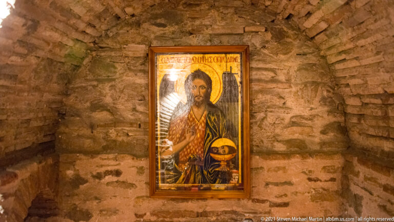 Framed Orthodox icon of Christ mounted on a rough wall of stone and brick masonry.