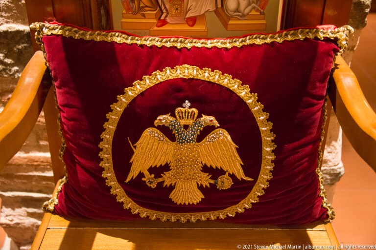 Gold embroidered double-headed eagle on a red velvet chair covering with ornate circular border.