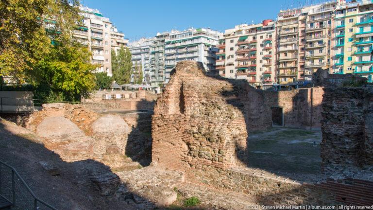 Excavated brick and stone ruins of Thessaloniki’s Roman Forum with apartment buildings surrounding the site.