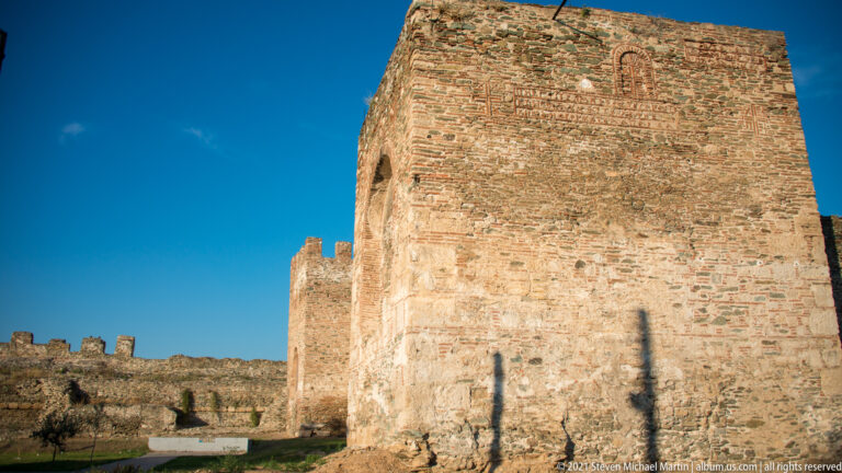 Low-angle view of broad brick-and-stone fortification tower with crenellated city wall extending behind.