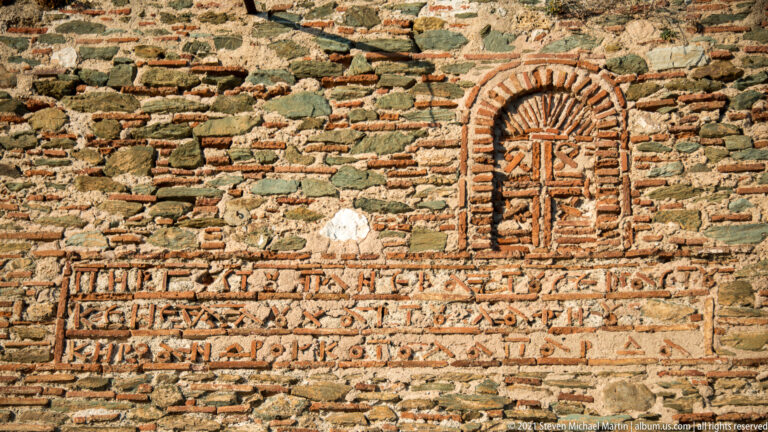 Close view of historic masonry with brick cross in an arched niche and patterned brick courses below.