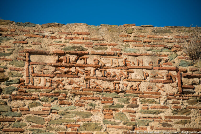 Close-up of reddish bricks arranged in inscription-like patterns within rough stone-and-brick fortification masonry.