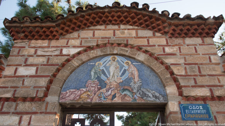 Semicircular Transfiguration mosaic with Christ in a blue mandorla and figures around him above a brick doorway.