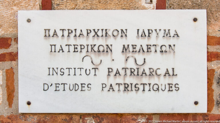 White marble plaque on brick wall naming the Patriarchal Institute for Patristic Studies in Greek and French.
