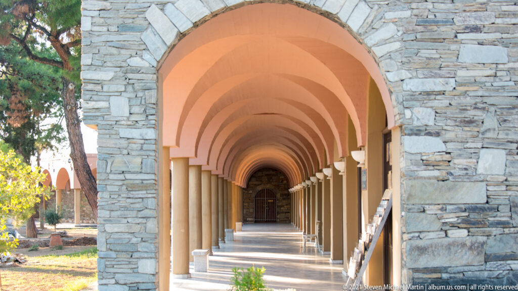 Covered arcaded walkway with repeated peach arches, slender columns, stone walls, and a dark doorway at the far end.