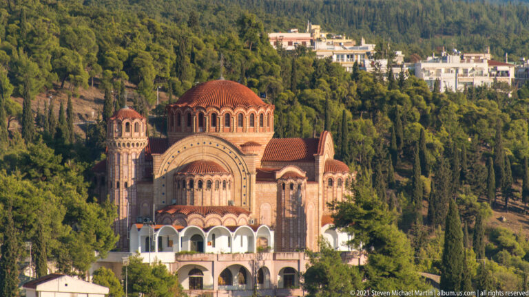 Large domed brick church among cypress trees and hillside houses in Thessaloniki's Upper Town.