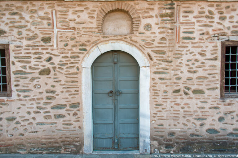 Blue-gray arched double door set in mixed brick-and-stone masonry with barred windows.