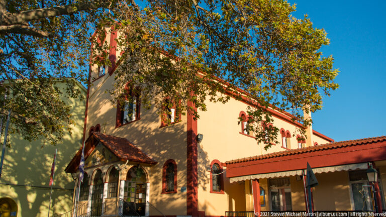 Yellow Orthodox church with red trim, arched windows, tiled roof, and trees in the foreground.