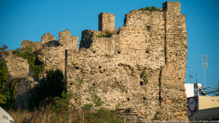 Ruined stone-and-brick acropolis wall with broken towers and vegetation along the crest.