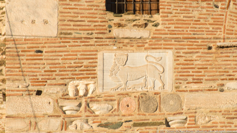 Rectangular marble relief of a walking lion reused among brick, stone, and carved fragments in a wall.