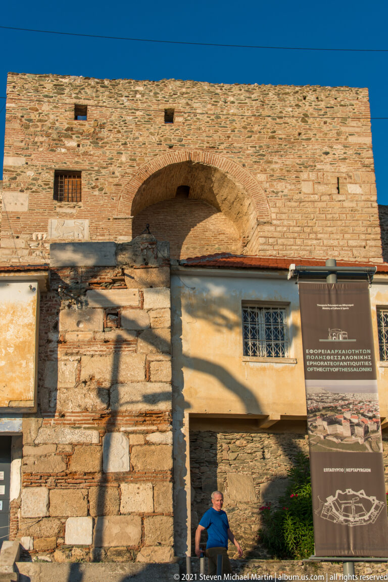 Low-angle view of a massive acropolis tower with arched recess, mixed masonry, and interpretive panels below.