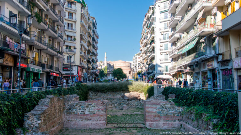 Long strip of excavated ancient brick foundations between apartment-lined streets in central Thessaloniki.