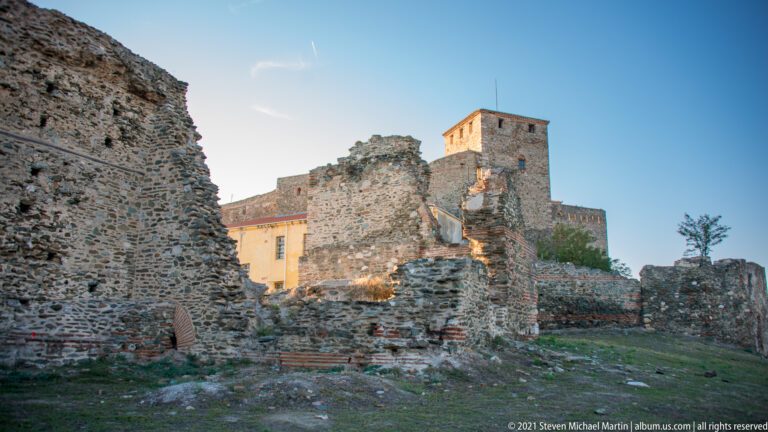 Fragmented stone-and-brick fortress ruins with a square tower and later building visible beyond.