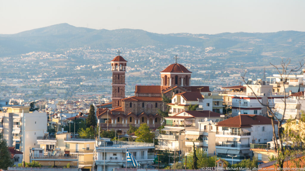 Large church with tall bell tower and red dome among hillside apartment buildings in Thessaloniki.