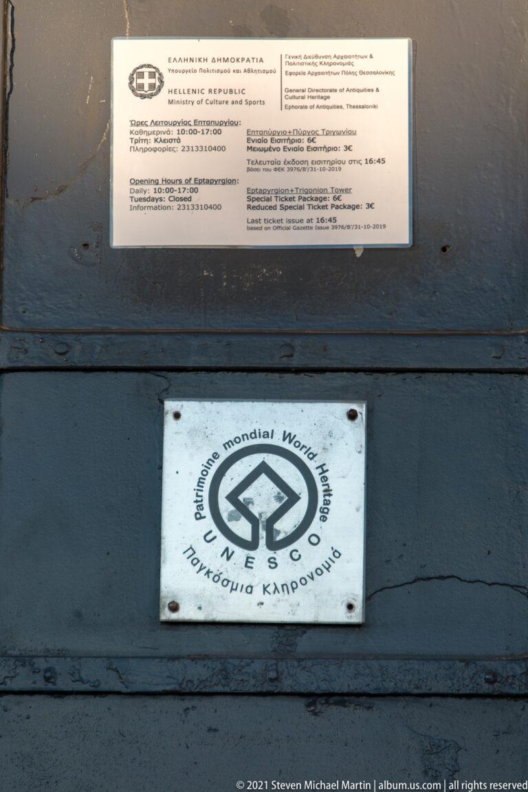 UNESCO World Heritage emblem mounted below a small information notice on a dark wall at Heptapyrgion.