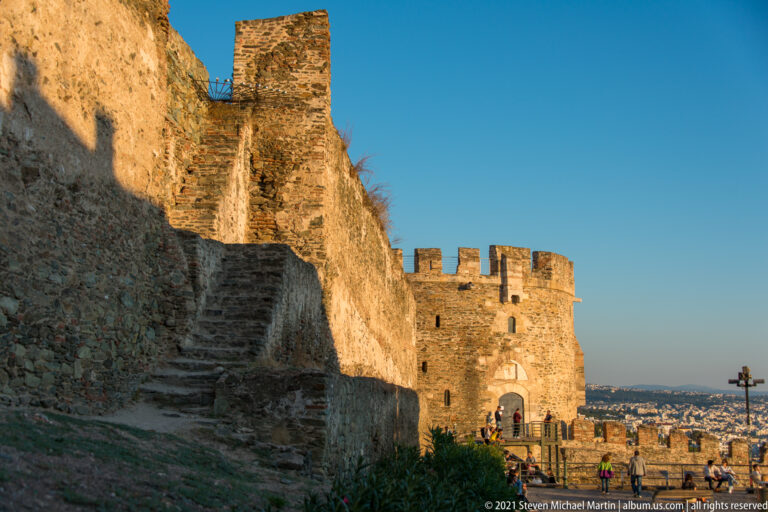 Stone stair beside a high masonry wall and crenellated tower overlooking Thessaloniki.