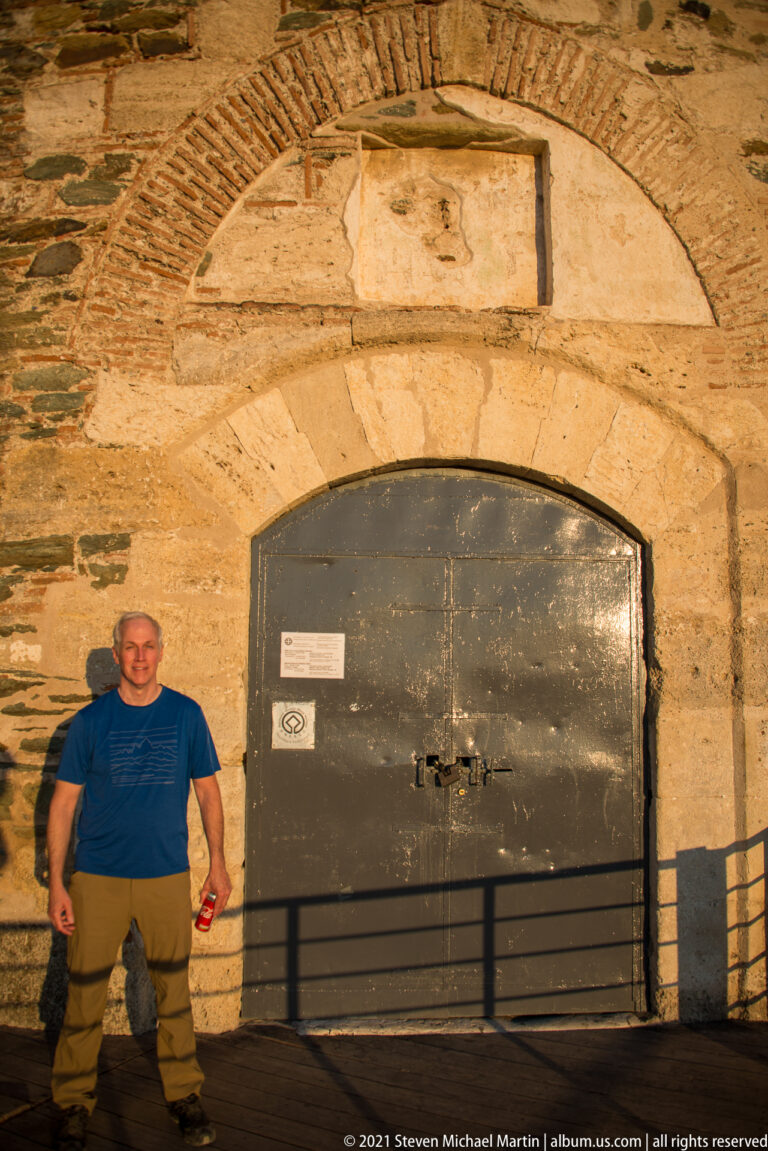 Visitor beside a dark metal door set in a broad stone-and-brick arch.