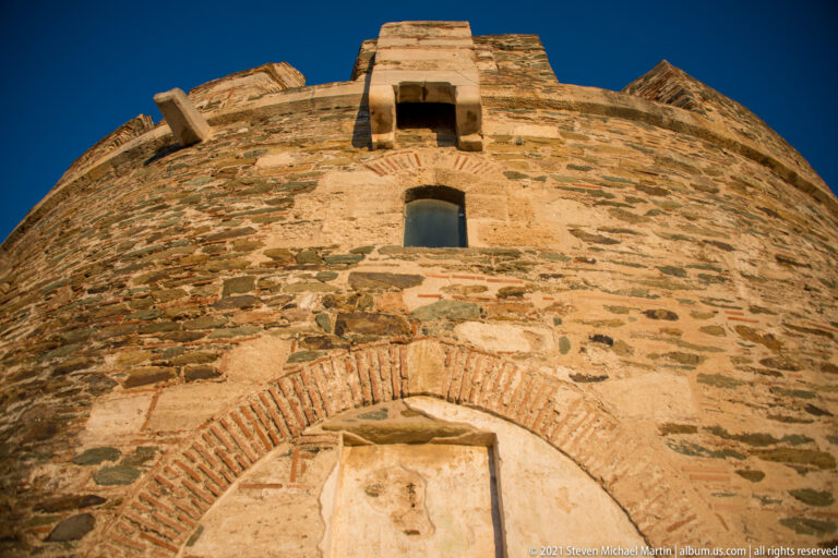 Low-angle close view of a stone-and-brick defensive tower against blue sky.