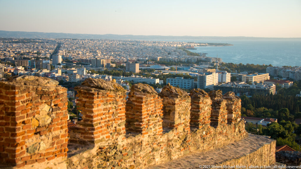 Weathered brick parapet in the foreground overlooking Thessaloniki and the Thermaic Gulf.