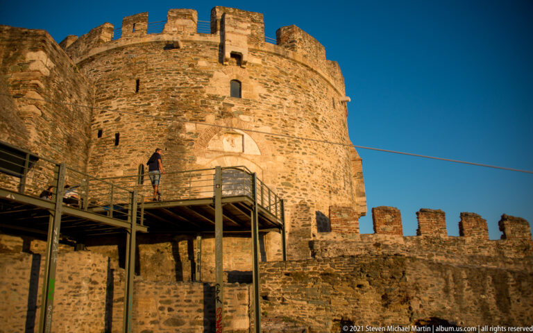 Crenellated stone tower beside a raised metal visitor walkway within Thessaloniki’s fortifications.