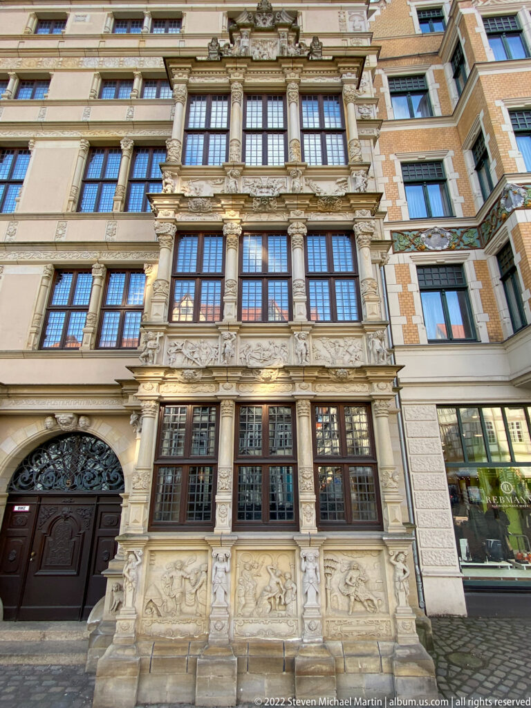 Narrow ornate stone façade with projecting windows, columns, carved figures, relief panels, and richly decorated horizontal bands.