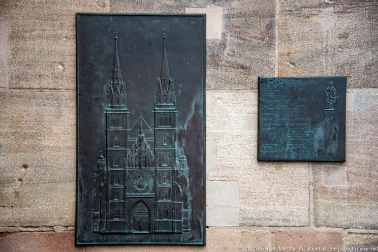 Bronze relief of St. Lorenz twin-towered west façade beside a smaller explanatory plaque.