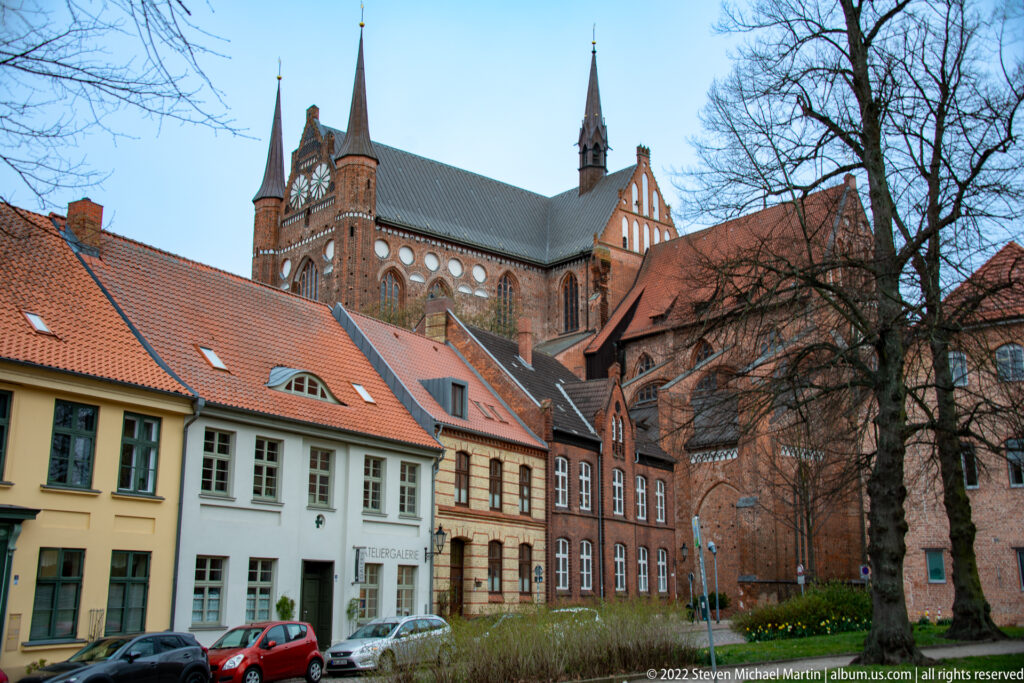 Large Brick Gothic church rising behind historic houses with red tile roofs in Wismar.