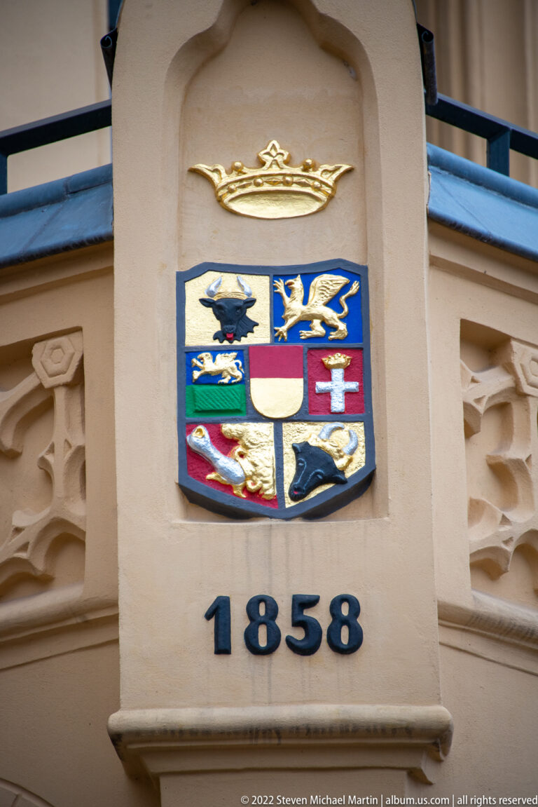 Colorful coat of arms mounted on a pale façade above the date 1858.