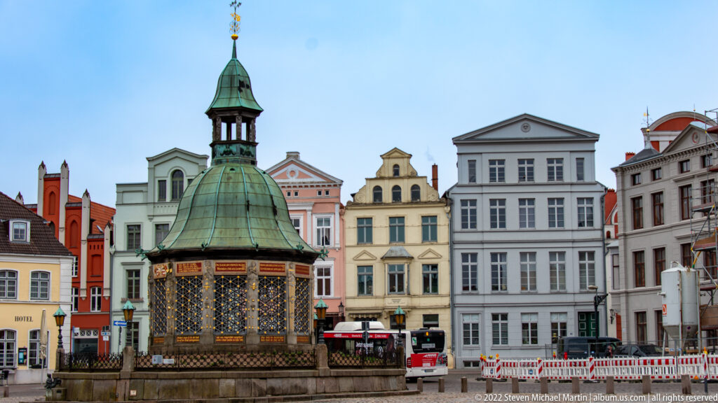 Wasserkunst pavilion with green copper dome and ornate sides in front of colorful market-square façades.