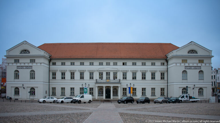 Long symmetrical pale town hall with red tile roof facing the open cobbled market square in Wismar.