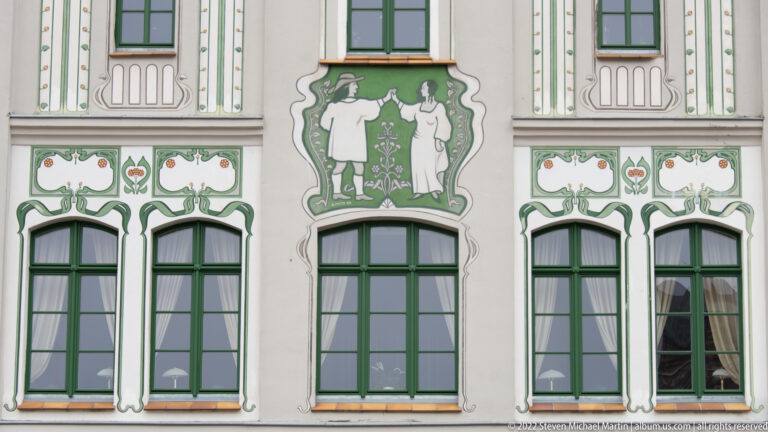Painted male and female figures above green-framed windows, surrounded by stylized green ornament.