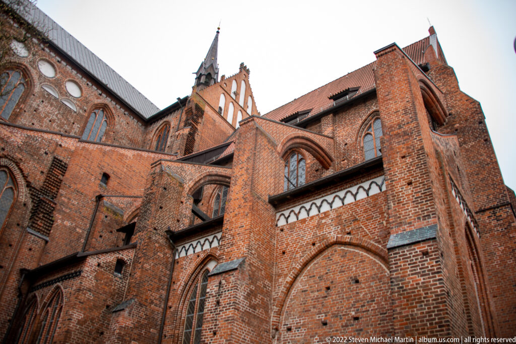 Close low-angle view of red-brick Gothic church walls, buttresses, pointed windows, and stepped gable.